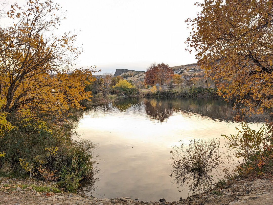 Auto-generated description: A serene lake is surrounded by trees with autumn foliage and rocky terrain, reflecting a tranquil landscape.