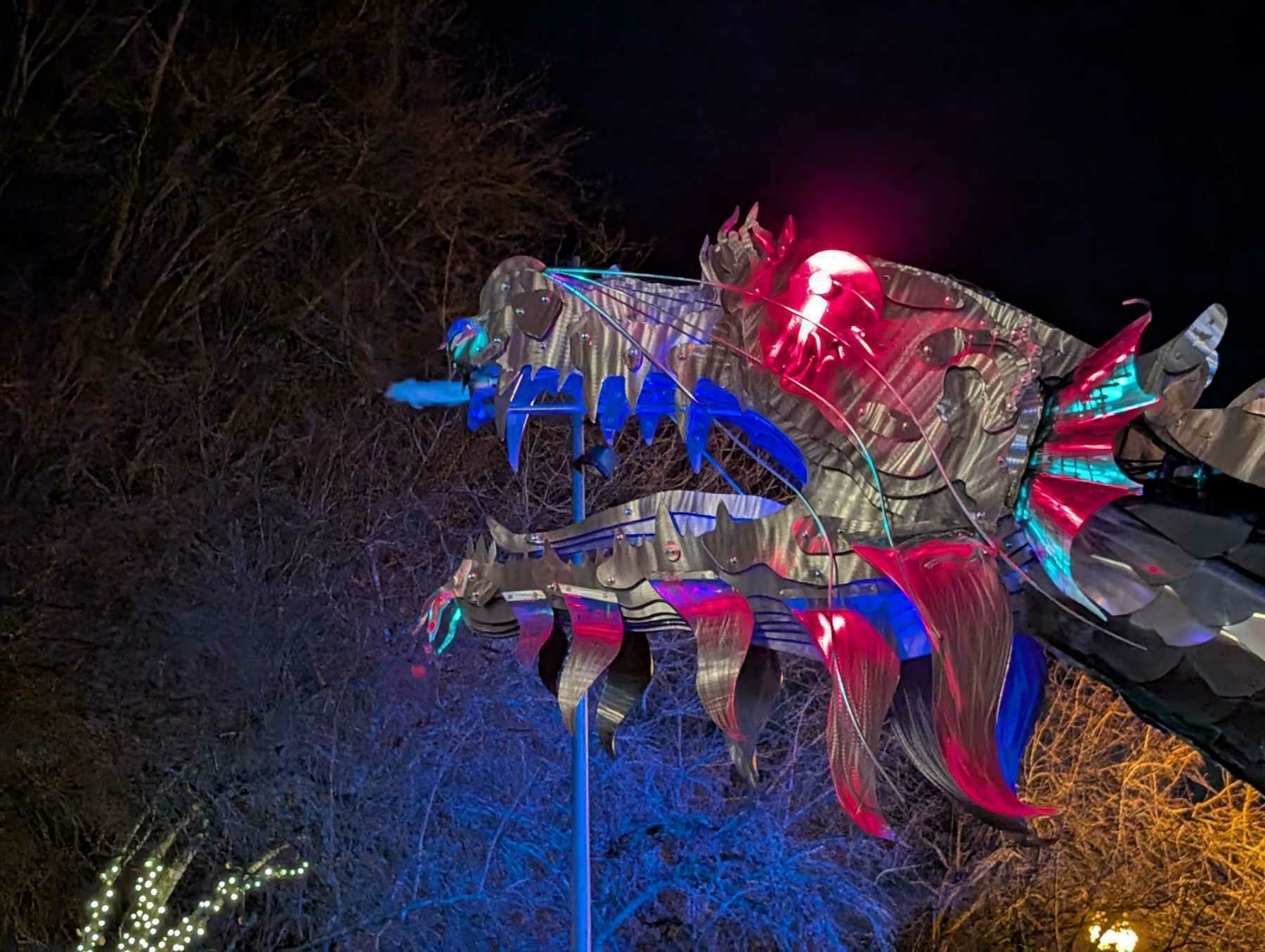 Auto-generated description: A vibrant, illuminated dragon sculpture is set against a dark, wooded background.