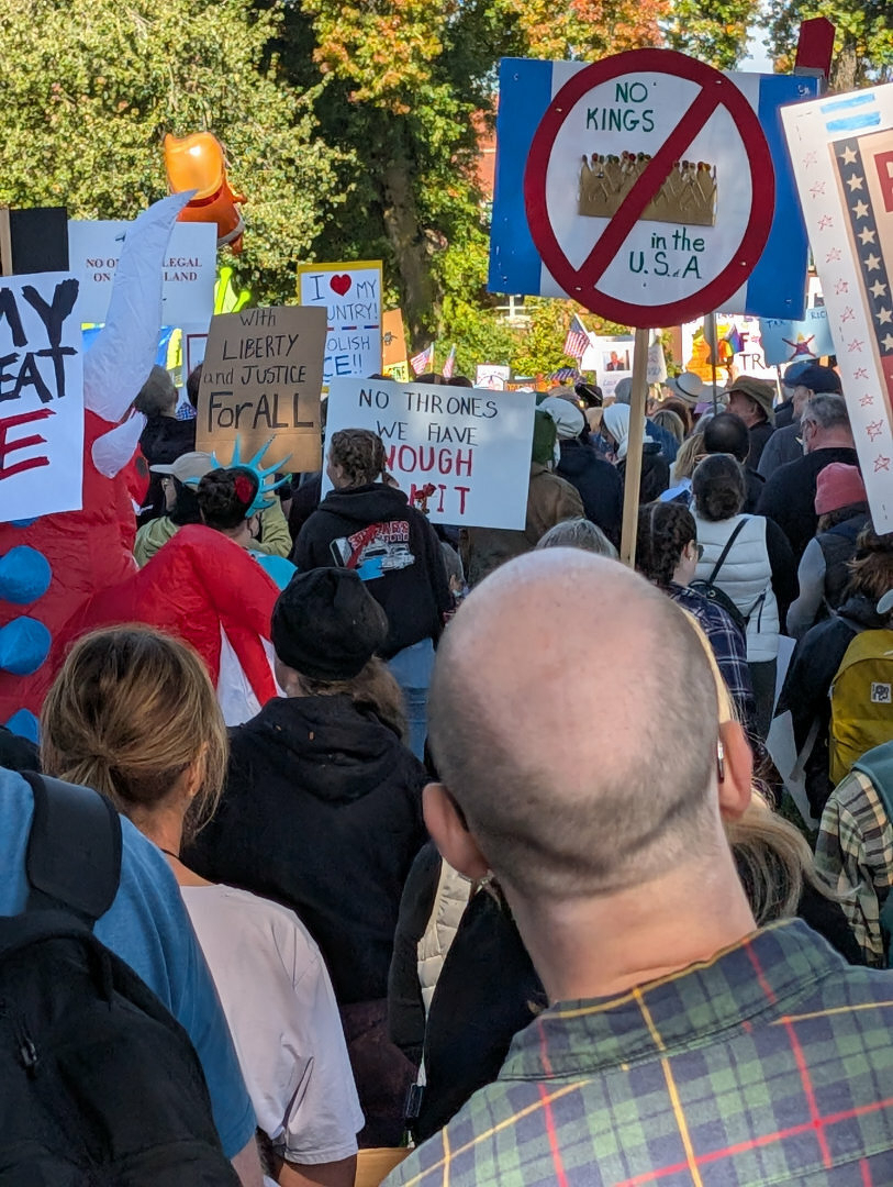 Auto-generated description: A crowd is gathered holding various signs related to justice and opposition to monarchic authority in the USA.