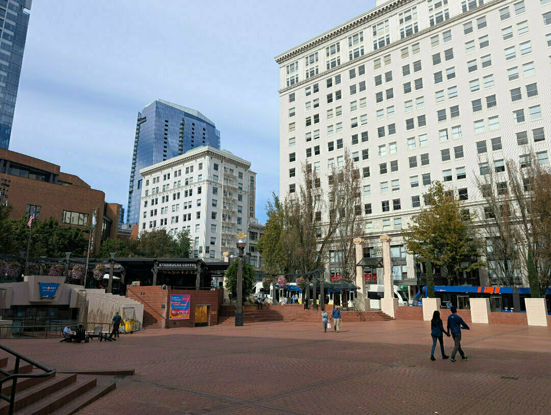 Auto-generated description: A large open plaza features a few pedestrians, surrounded by tall buildings and trees.