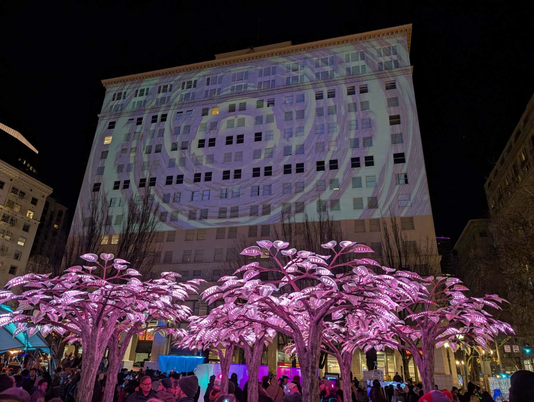 A water scene projected onto a large building over a forest made of light.