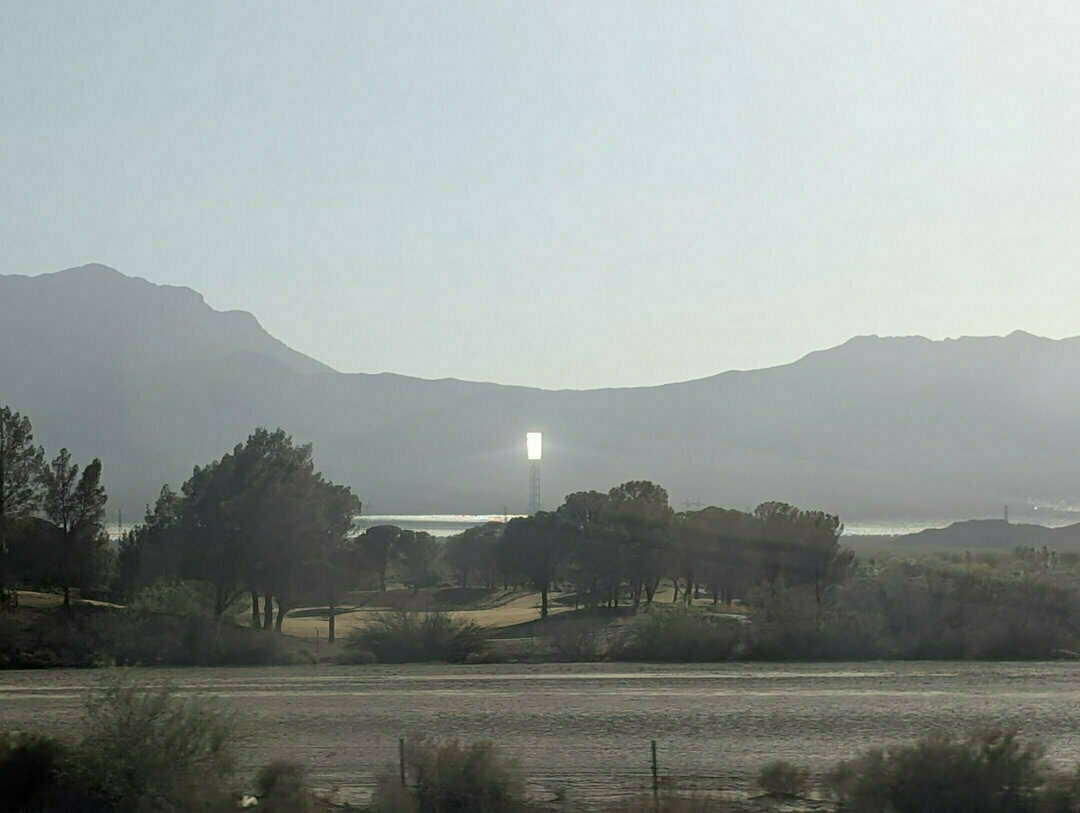 Auto-generated description: A tall, bright reflective structure stands amidst a desert landscape with mountains and trees.