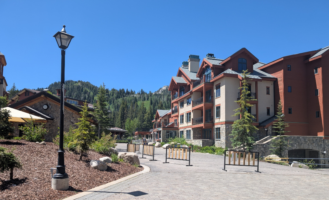 Auto-generated description: A mountain resort with multi-story buildings is set against a lush, forested backdrop under a clear blue sky.