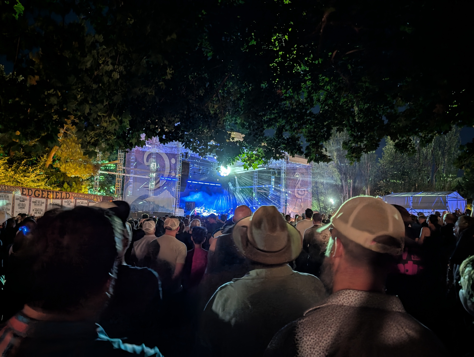 A large crowd watches a brightly lit stage during an outdoor nighttime concert.