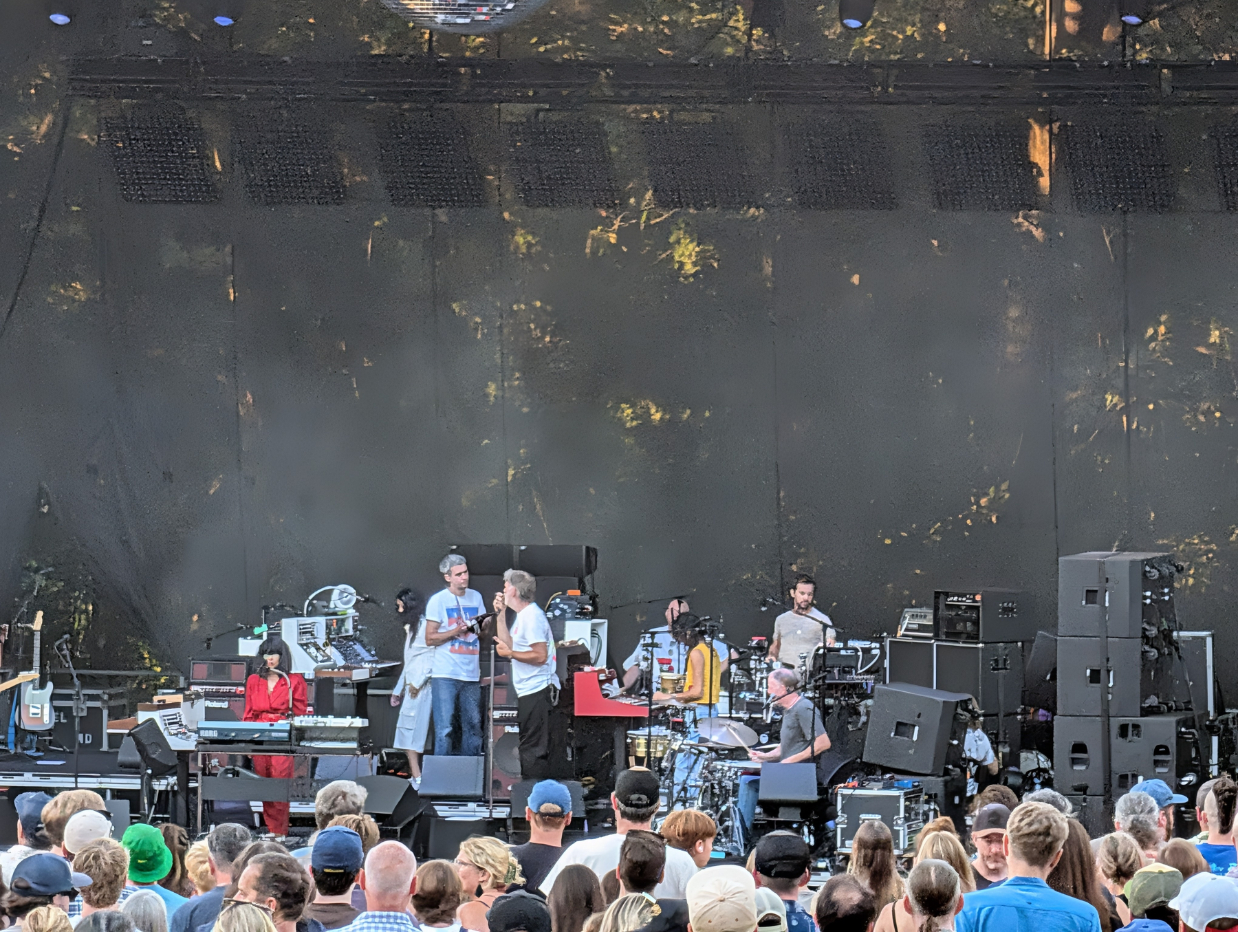 A band is performing on stage in front of a large crowd at an outdoor event.