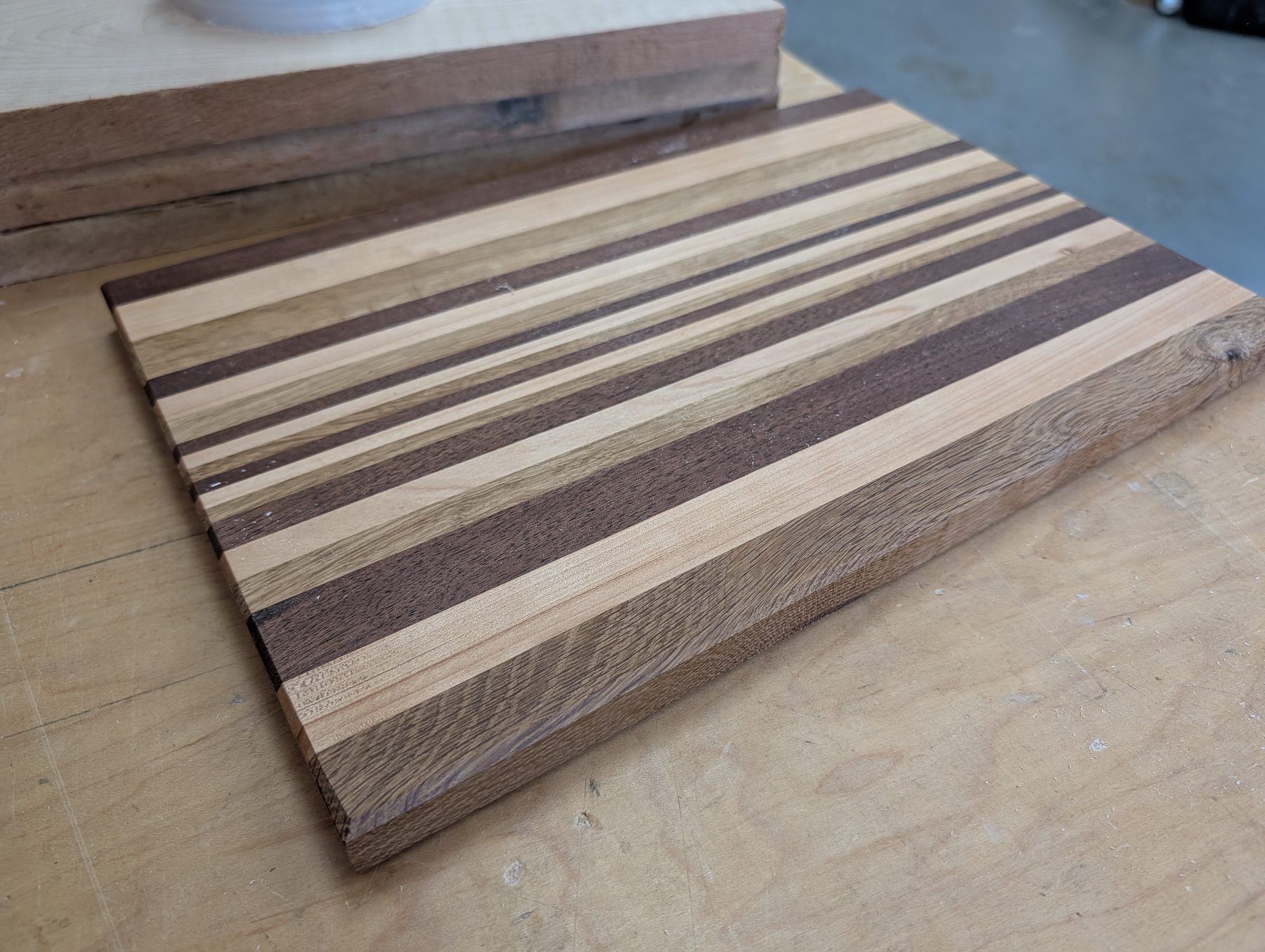 Auto-generated description: A wooden cutting board features alternating light and dark stripes arranged horizontally on a workbench.