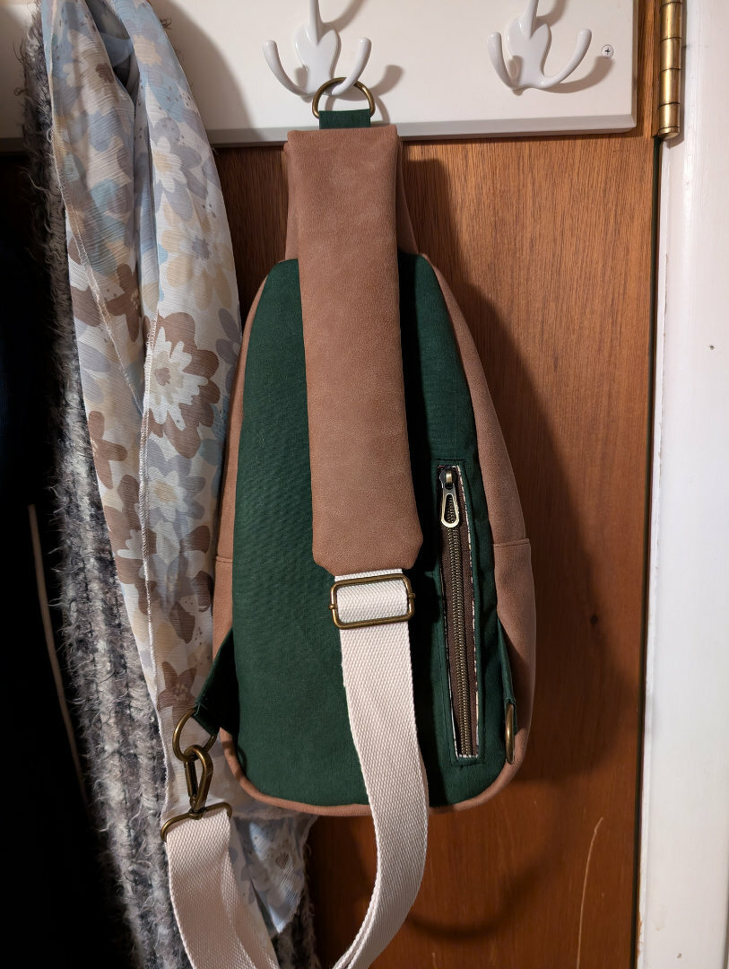 Auto-generated description: A backpack with a green body and brown accents is hanging from hooks on a wooden door, next to a floral-patterned scarf.