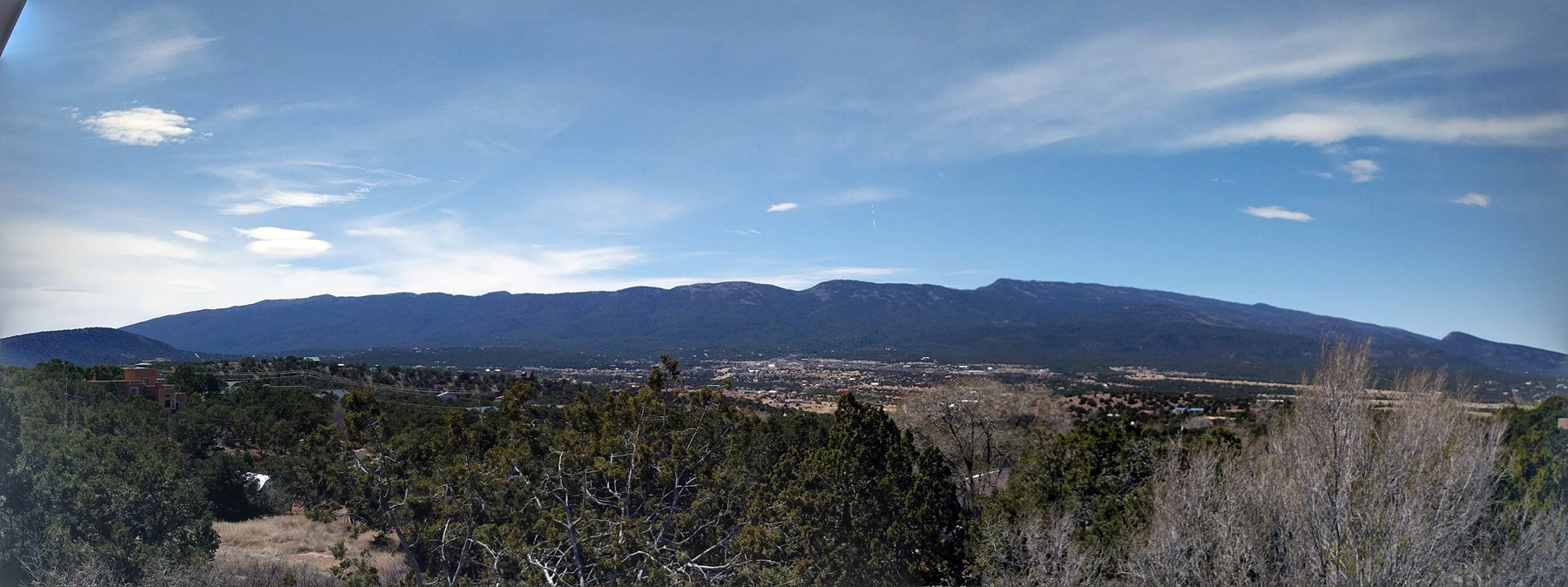 Auto-generated description: A vast landscape features a panoramic view of forested hills leading up to a distant mountain range under a partly cloudy sky.